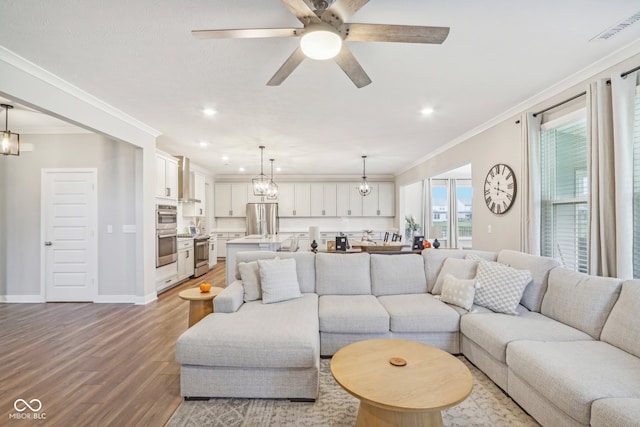 living room with wood-type flooring, ceiling fan with notable chandelier, and ornamental molding