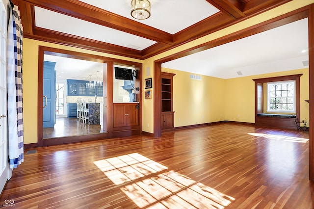 unfurnished living room with beam ceiling, coffered ceiling, an inviting chandelier, ornamental molding, and hardwood / wood-style flooring