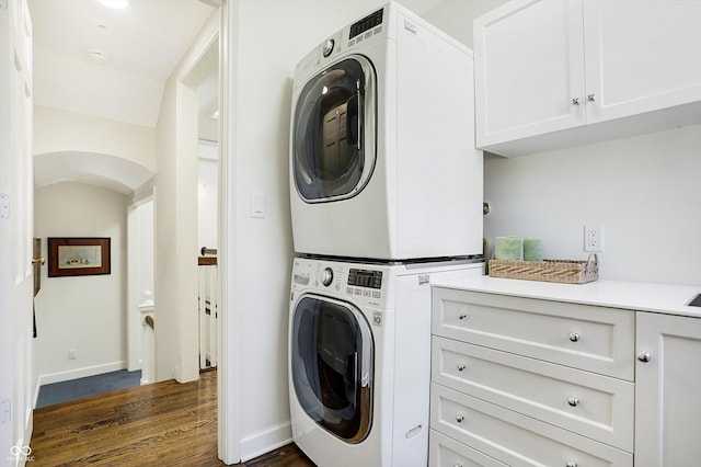 2505 Riverside Dr, Columbus, IN 47201 - washroom featuring stacked washer and clothes dryer, cabinet space, dark wood-style flooring, baseboards, and arched walkways
