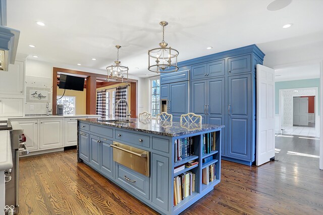 kitchen featuring blue cabinetry, sink, dark hardwood / wood-style flooring, dark stone countertops, and an island with sink