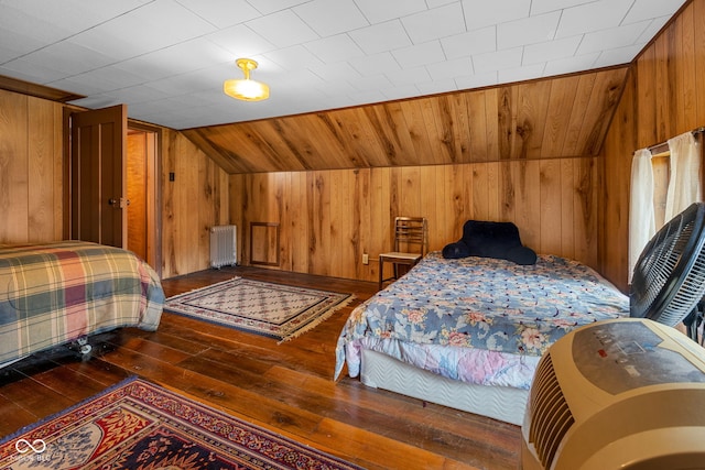 bedroom with dark hardwood / wood-style flooring, radiator, wooden walls, and vaulted ceiling