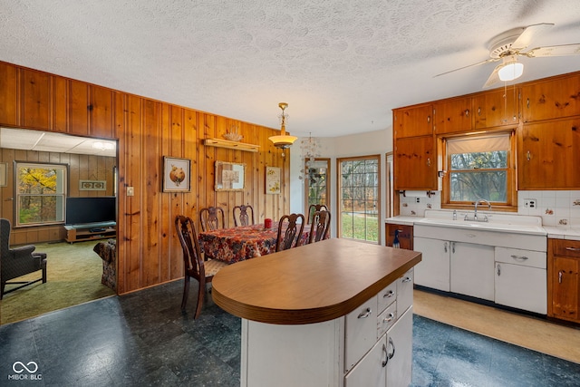 kitchen featuring white cabinetry, sink, wooden walls, and decorative light fixtures