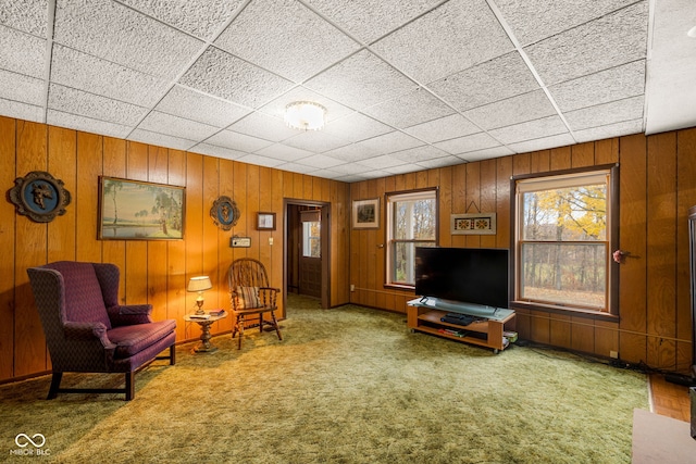 unfurnished living room with a paneled ceiling, wooden walls, and carpet flooring