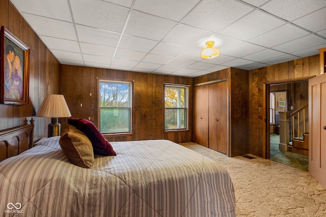 bedroom featuring carpet floors, a drop ceiling, wooden walls, and a closet