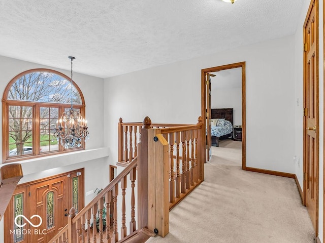 hallway with a chandelier, light carpet, and a textured ceiling