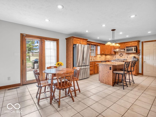 kitchen with backsplash, stainless steel appliances, light tile patterned floors, decorative light fixtures, and a kitchen island