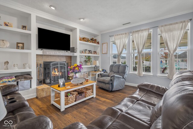 living room featuring dark hardwood / wood-style floors, a tile fireplace, ornamental molding, built in features, and a textured ceiling