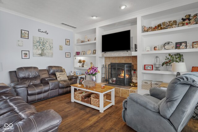 living room with crown molding, a tiled fireplace, built in shelves, and dark hardwood / wood-style flooring