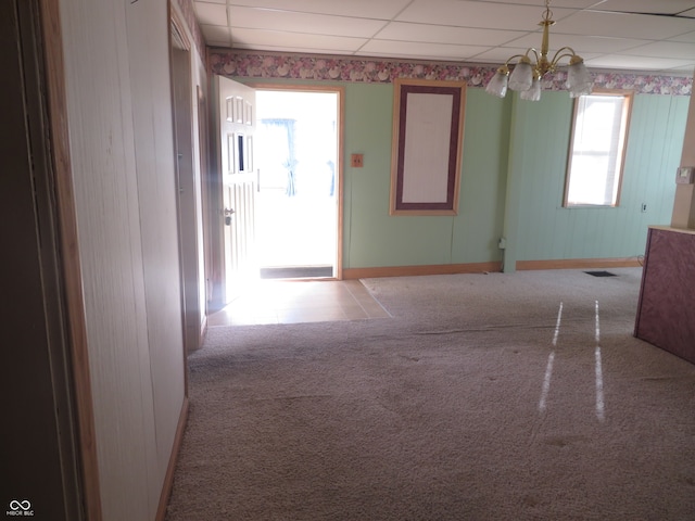 hall with light carpet, a drop ceiling, and a notable chandelier