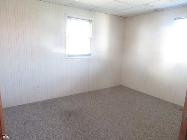 unfurnished room featuring a paneled ceiling, wooden walls, and a wealth of natural light