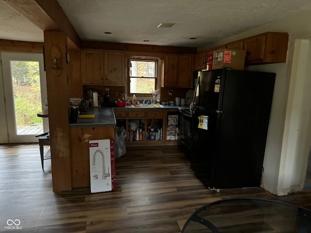 kitchen with dark hardwood / wood-style floors, a textured ceiling, black refrigerator, and sink