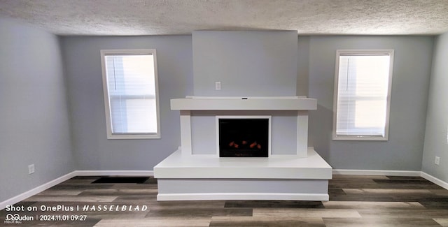 unfurnished living room with a textured ceiling, a healthy amount of sunlight, and dark wood-type flooring