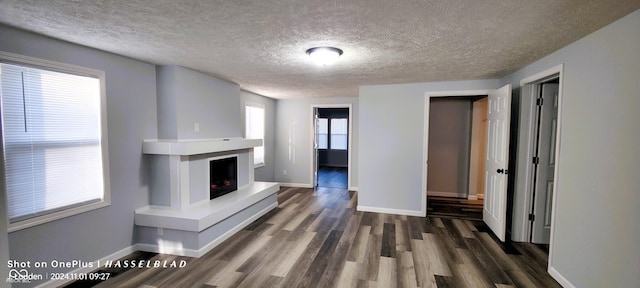 12544 S State Road 3, Westport, IN 47283 - unfurnished living room featuring baseboards, a textured ceiling, dark wood-style floors, and a fireplace with raised hearth
