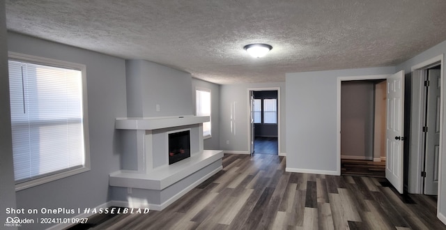 12544 S State Road 3, Westport, IN 47283 - unfurnished living room with dark wood-style flooring, baseboards, a textured ceiling, and a fireplace with raised hearth