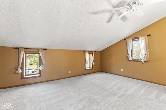 additional living space featuring lofted ceiling, a textured ceiling, light colored carpet, and plenty of natural light