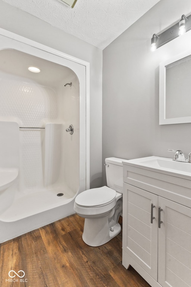 bathroom with toilet, wood-type flooring, a shower, vanity, and a textured ceiling