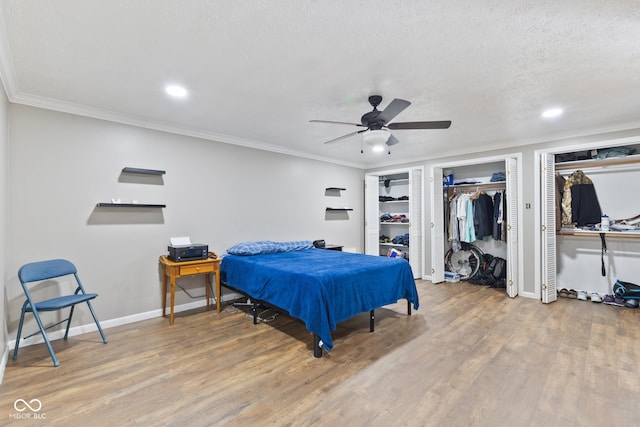 bedroom featuring wood-type flooring, ornamental molding, two closets, a textured ceiling, and ceiling fan