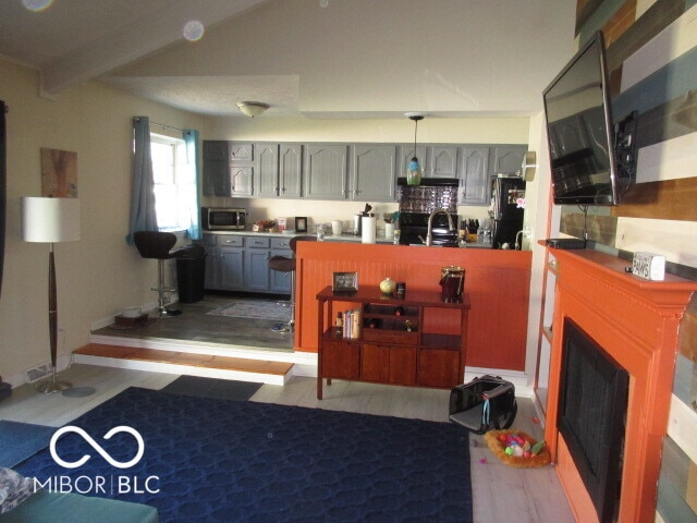 kitchen with gray cabinetry, fridge, light hardwood / wood-style floors, black / electric stove, and beam ceiling