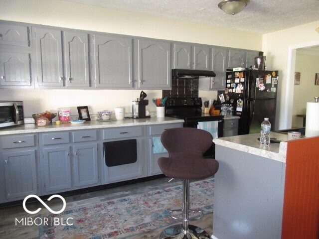 kitchen featuring dark wood-type flooring, black appliances, a textured ceiling, and ventilation hood