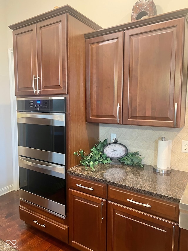 kitchen with dark stone counters, dark hardwood / wood-style floors, decorative backsplash, and double oven