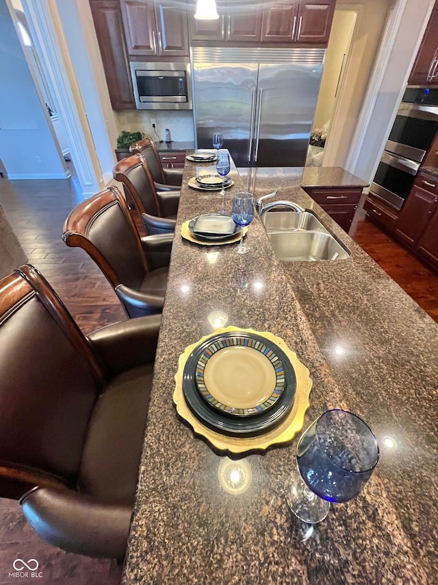 kitchen featuring built in appliances, dark hardwood / wood-style floors, sink, and dark stone countertops