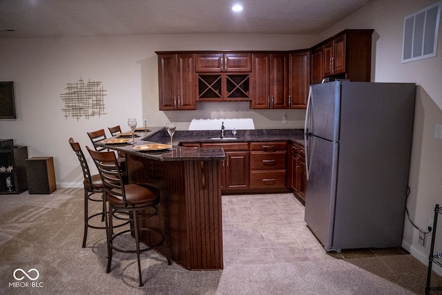 kitchen with dark stone counters, light carpet, sink, a breakfast bar area, and stainless steel refrigerator