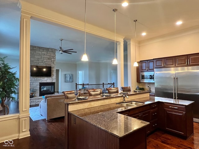 kitchen with a stone fireplace, decorative light fixtures, built in appliances, dark hardwood / wood-style flooring, and sink