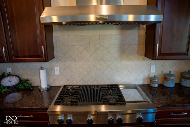 kitchen with dark brown cabinetry, wall chimney exhaust hood, tasteful backsplash, and dark stone countertops