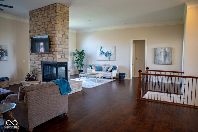 living room with dark wood-type flooring, a stone fireplace, and ornamental molding