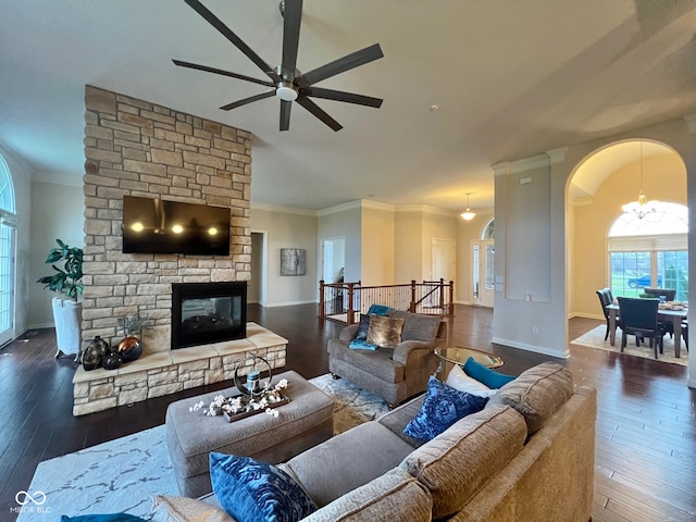 living room with a stone fireplace, ceiling fan with notable chandelier, dark hardwood / wood-style floors, and crown molding