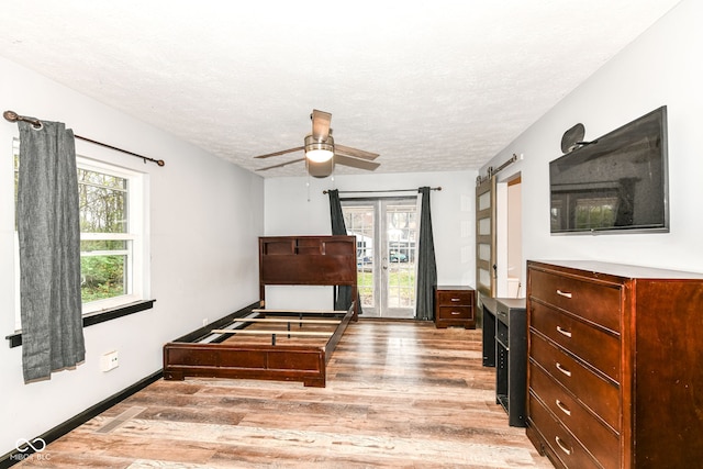 bedroom with a textured ceiling, access to outside, ceiling fan, a barn door, and light hardwood / wood-style flooring