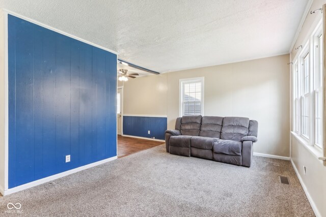 carpeted living room with ceiling fan, a textured ceiling, and wooden walls