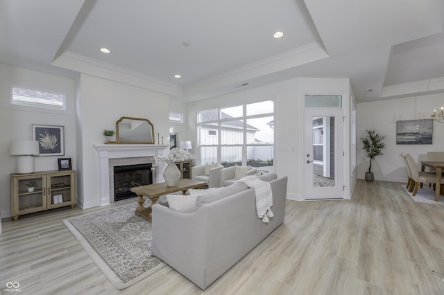 living area with a glass covered fireplace, a tray ceiling, crown molding, light wood-type flooring, and recessed lighting