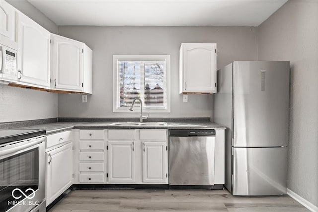 kitchen featuring a sink, white cabinetry, appliances with stainless steel finishes, light wood finished floors, and dark countertops