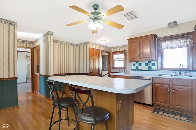 kitchen with a breakfast bar, stainless steel dishwasher, a healthy amount of sunlight, and light wood-type flooring