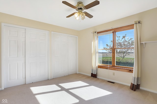 unfurnished bedroom featuring ceiling fan, light colored carpet, and multiple closets