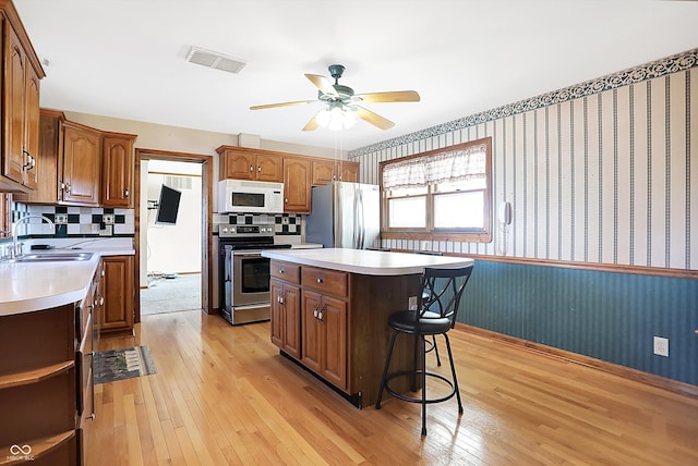 kitchen featuring stainless steel appliances, light hardwood / wood-style floors, sink, ceiling fan, and a kitchen island