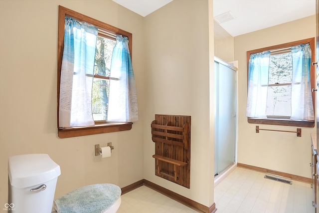 bathroom with toilet, a shower with shower door, and plenty of natural light