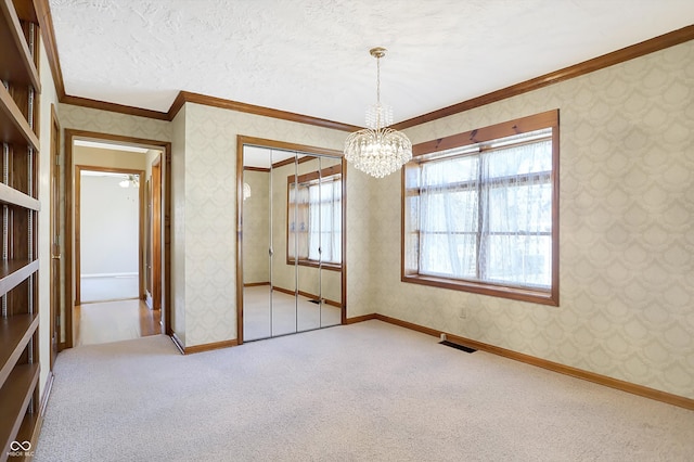 spare room with a textured ceiling, carpet flooring, crown molding, and a notable chandelier