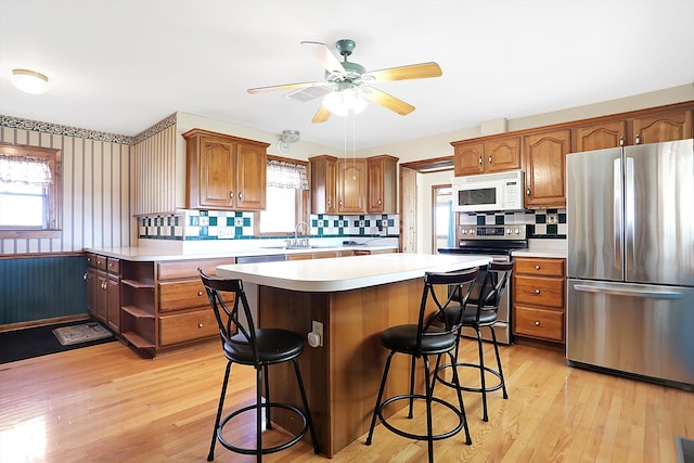 kitchen with stainless steel appliances, light hardwood / wood-style floors, sink, tasteful backsplash, and a kitchen island