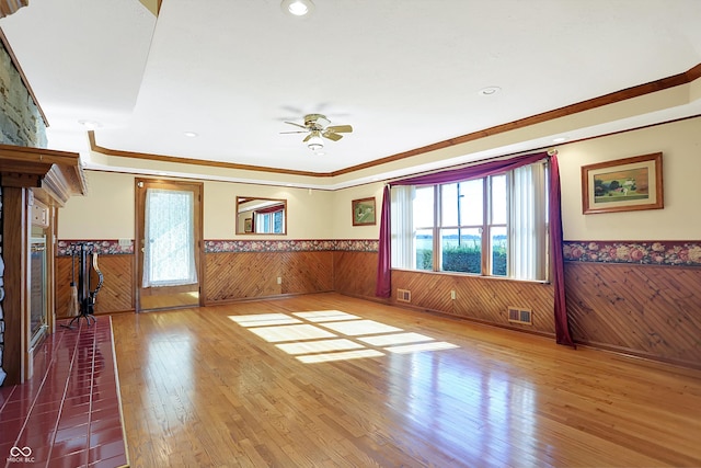 unfurnished living room featuring hardwood / wood-style flooring, ceiling fan, wooden walls, and crown molding