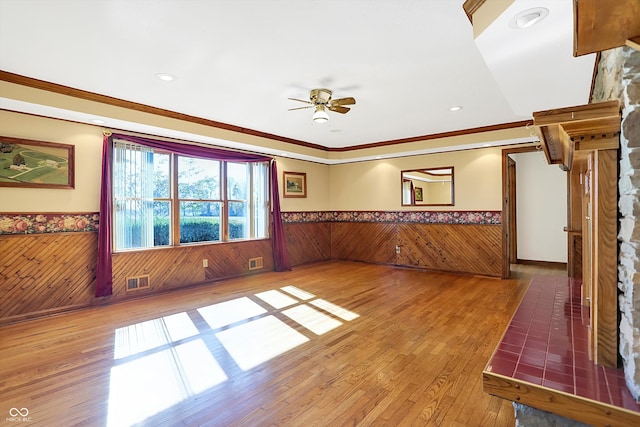 unfurnished living room featuring hardwood / wood-style floors, wooden walls, ceiling fan, and crown molding