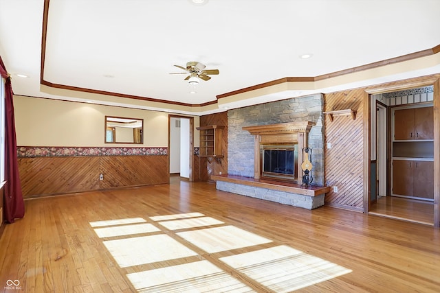 unfurnished living room featuring a stone fireplace, wood-type flooring, crown molding, and wood walls