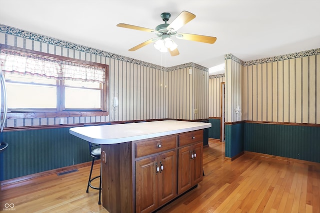 kitchen featuring light wood-type flooring, ceiling fan, a breakfast bar, and a center island