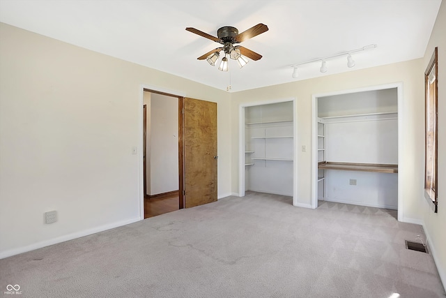 unfurnished bedroom featuring ceiling fan, rail lighting, multiple closets, and light colored carpet