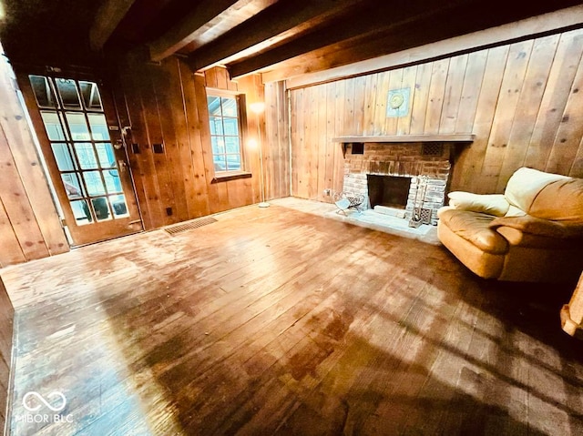 unfurnished room with wood walls, hardwood / wood-style flooring, beamed ceiling, and a brick fireplace