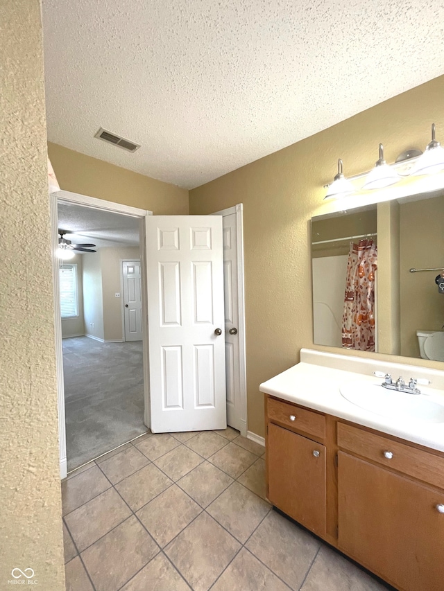 bathroom with toilet, tile patterned flooring, vanity, a textured ceiling, and ceiling fan