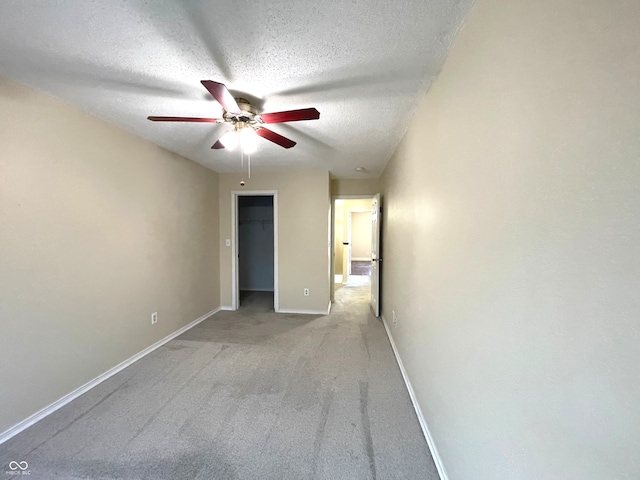 unfurnished bedroom featuring a closet, carpet floors, a spacious closet, a textured ceiling, and ceiling fan