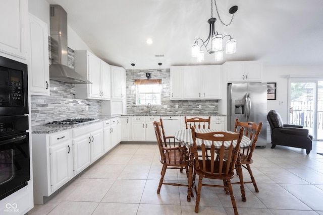 kitchen with black appliances, wall chimney range hood, decorative light fixtures, and plenty of natural light