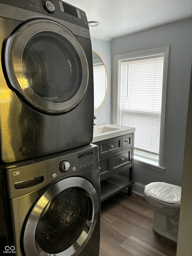 laundry area featuring stacked washer / dryer, sink, and dark hardwood / wood-style flooring